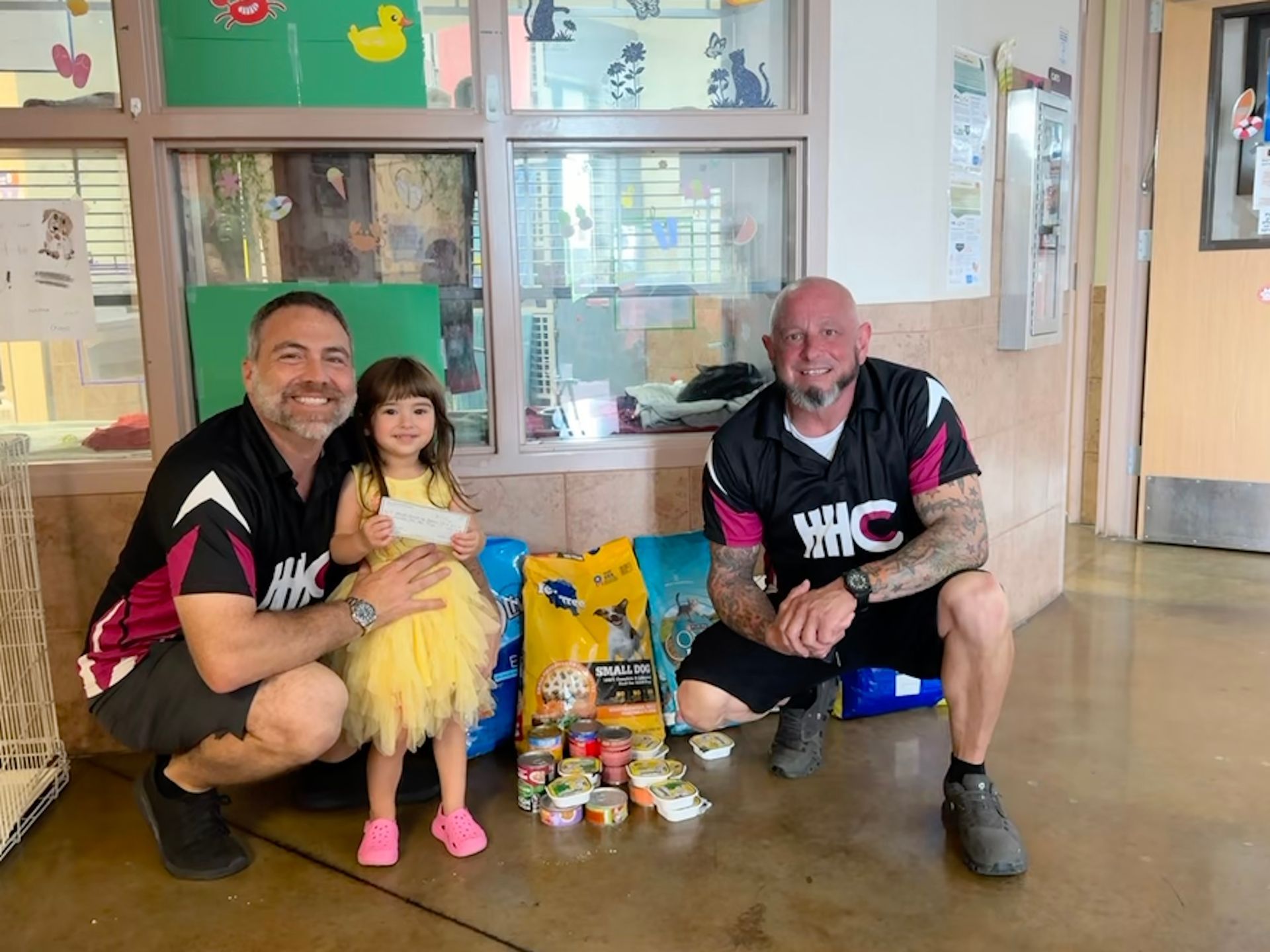 Two men and a girl donate pet food at a shelter.