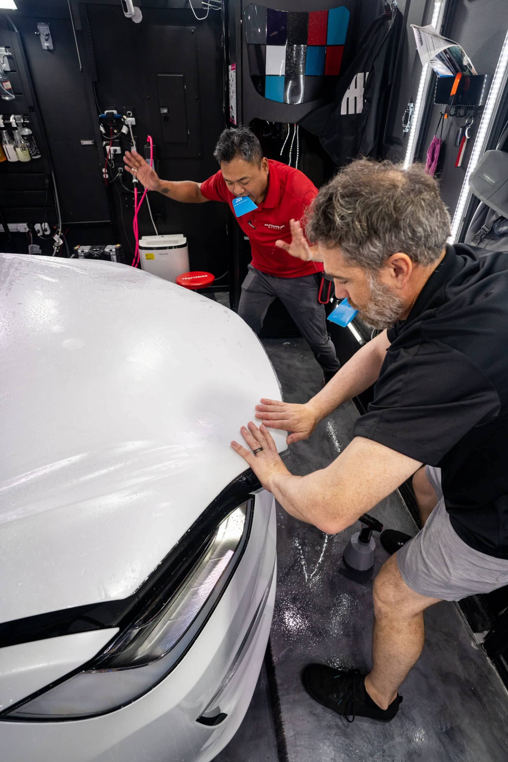 Two men are working on a white car in a garage.