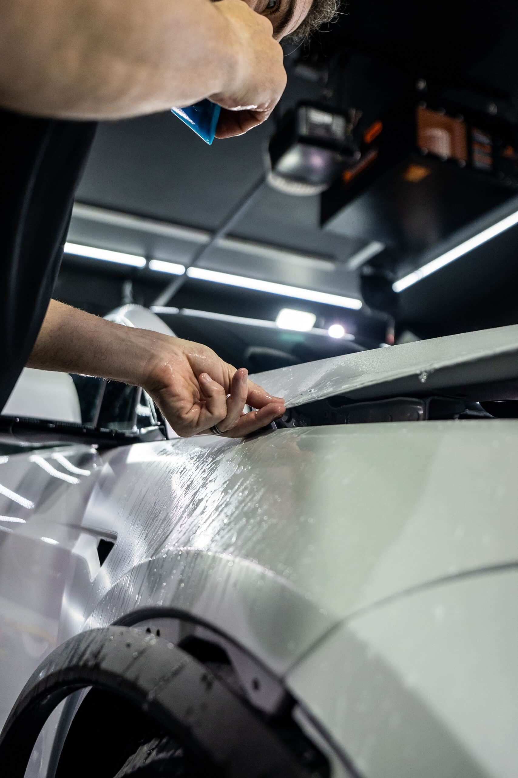 A man is applying a protective film to the fender of a white car.