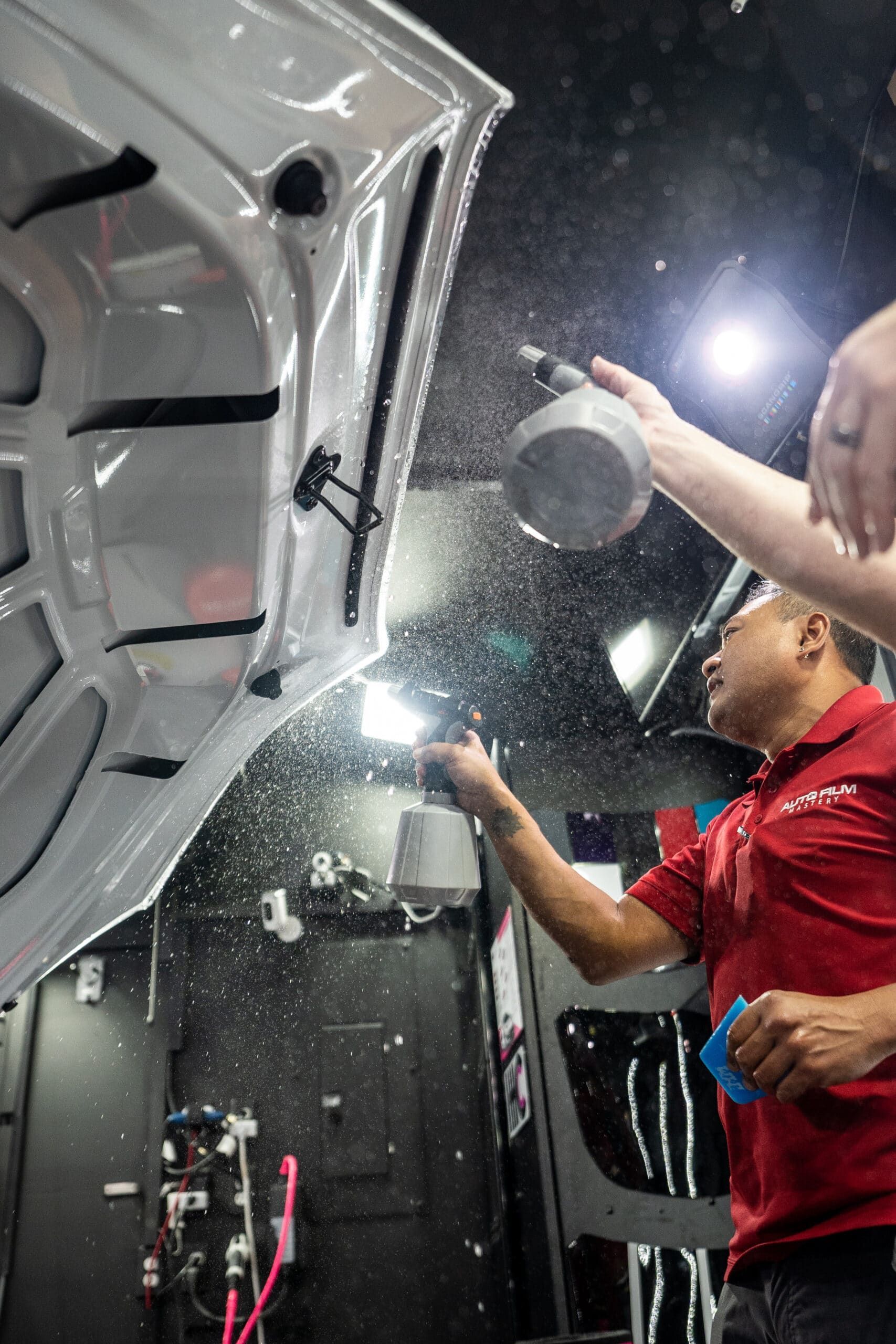 A man in a red shirt is spraying a car with a spray bottle.