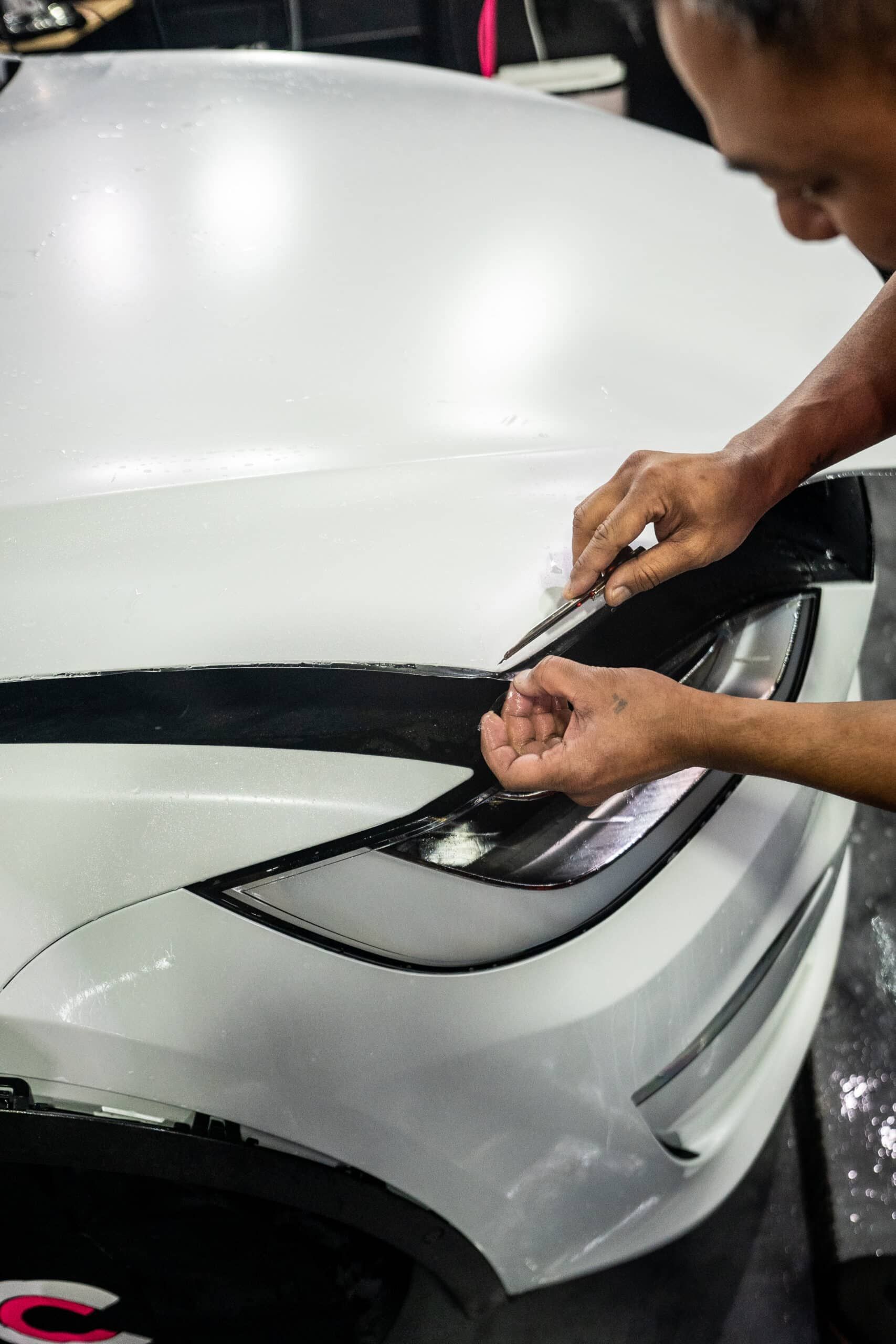 A man is wrapping a white car with plastic wrap.