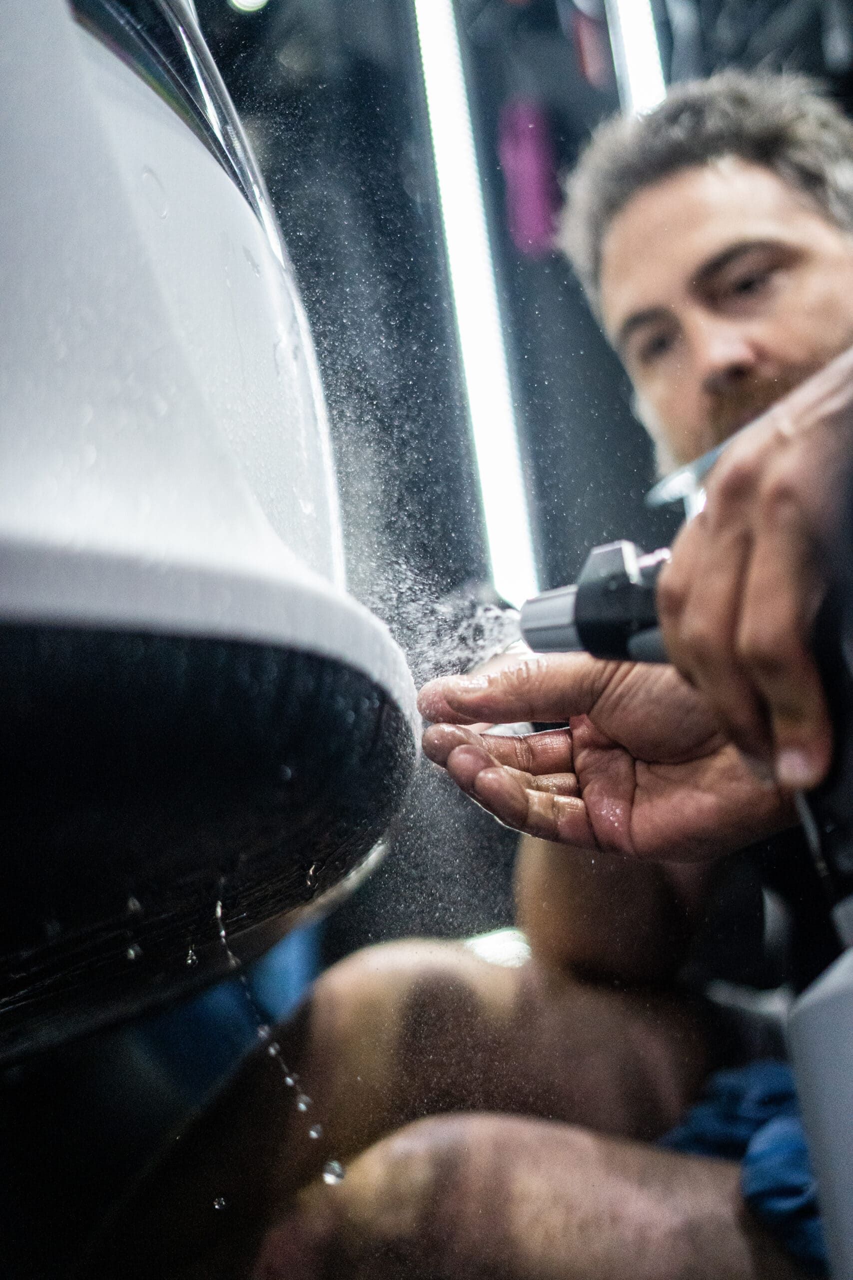 A man is spraying water on a white car.