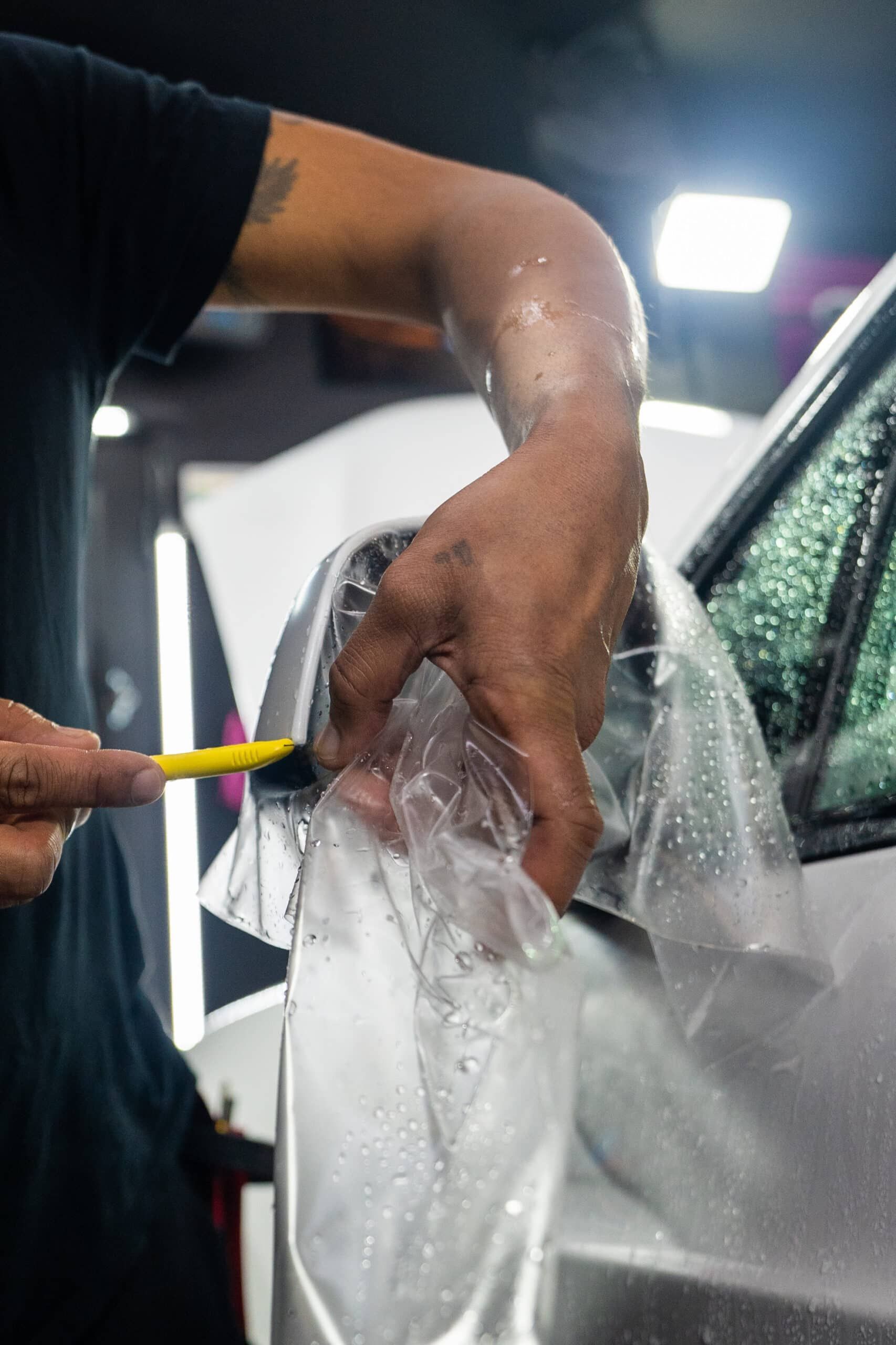 A man is applying a protective film to the side of a car.