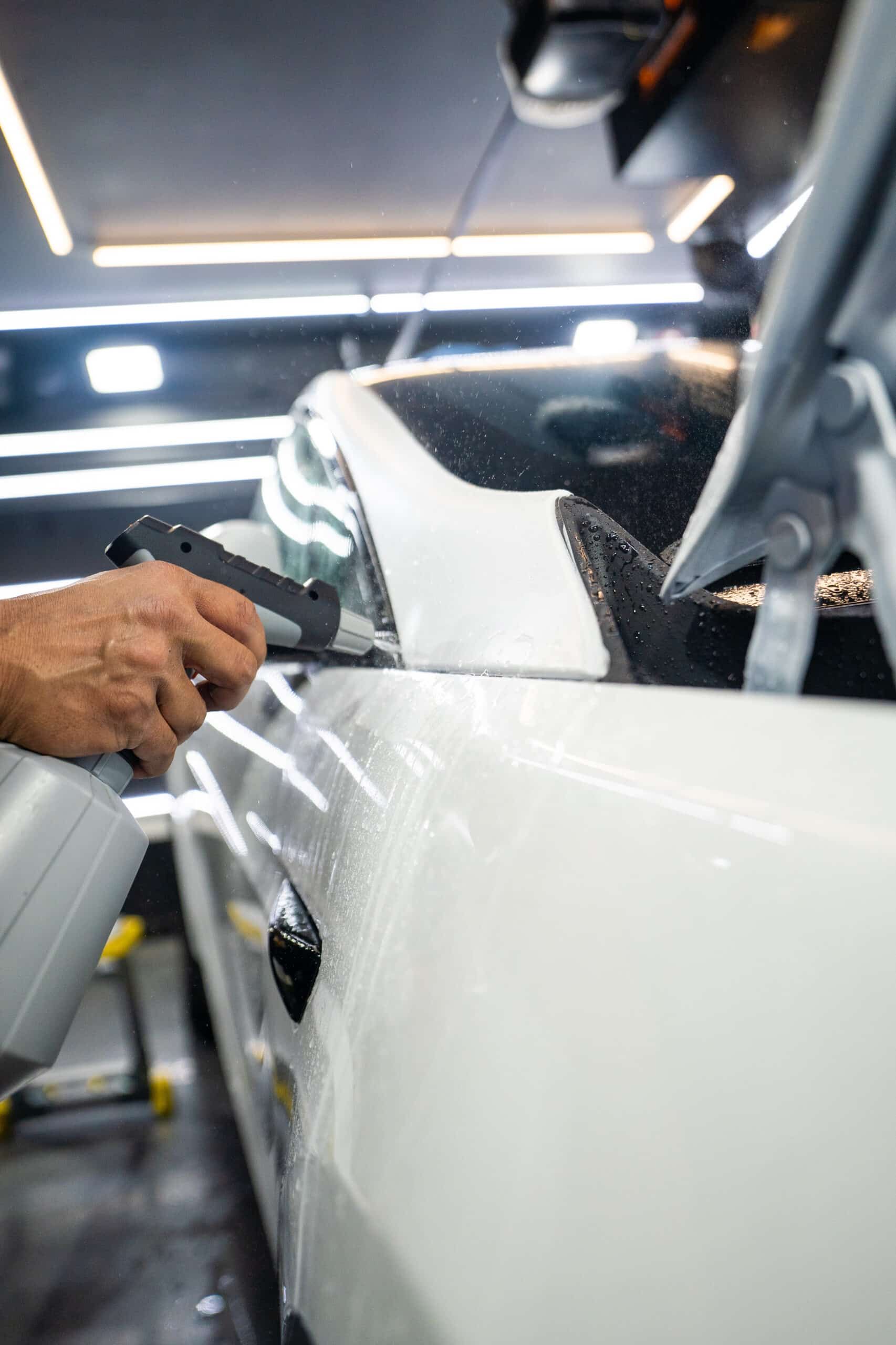 A man is polishing the side of a white car in a garage.