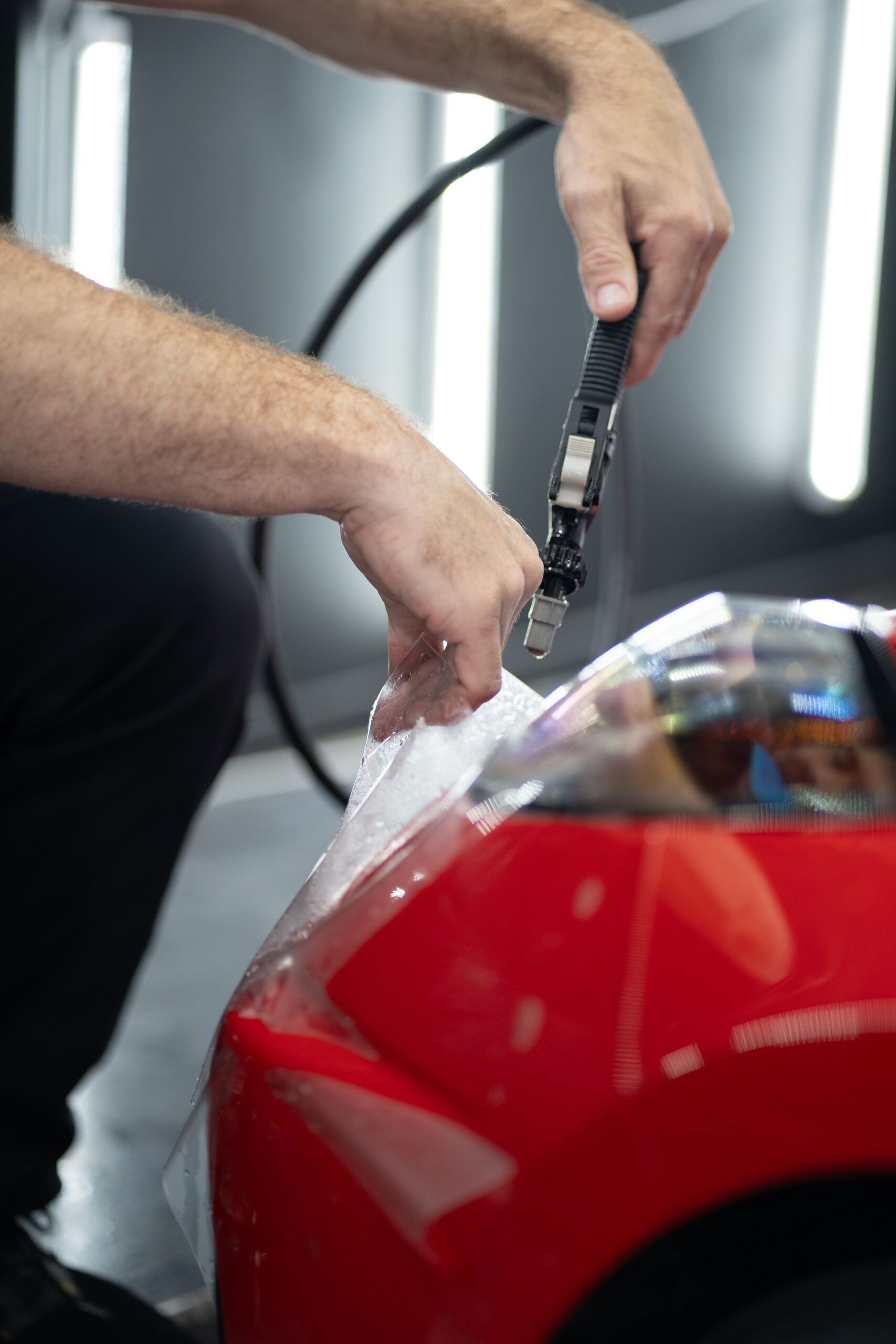 A man is cutting a piece of plastic on a red car.