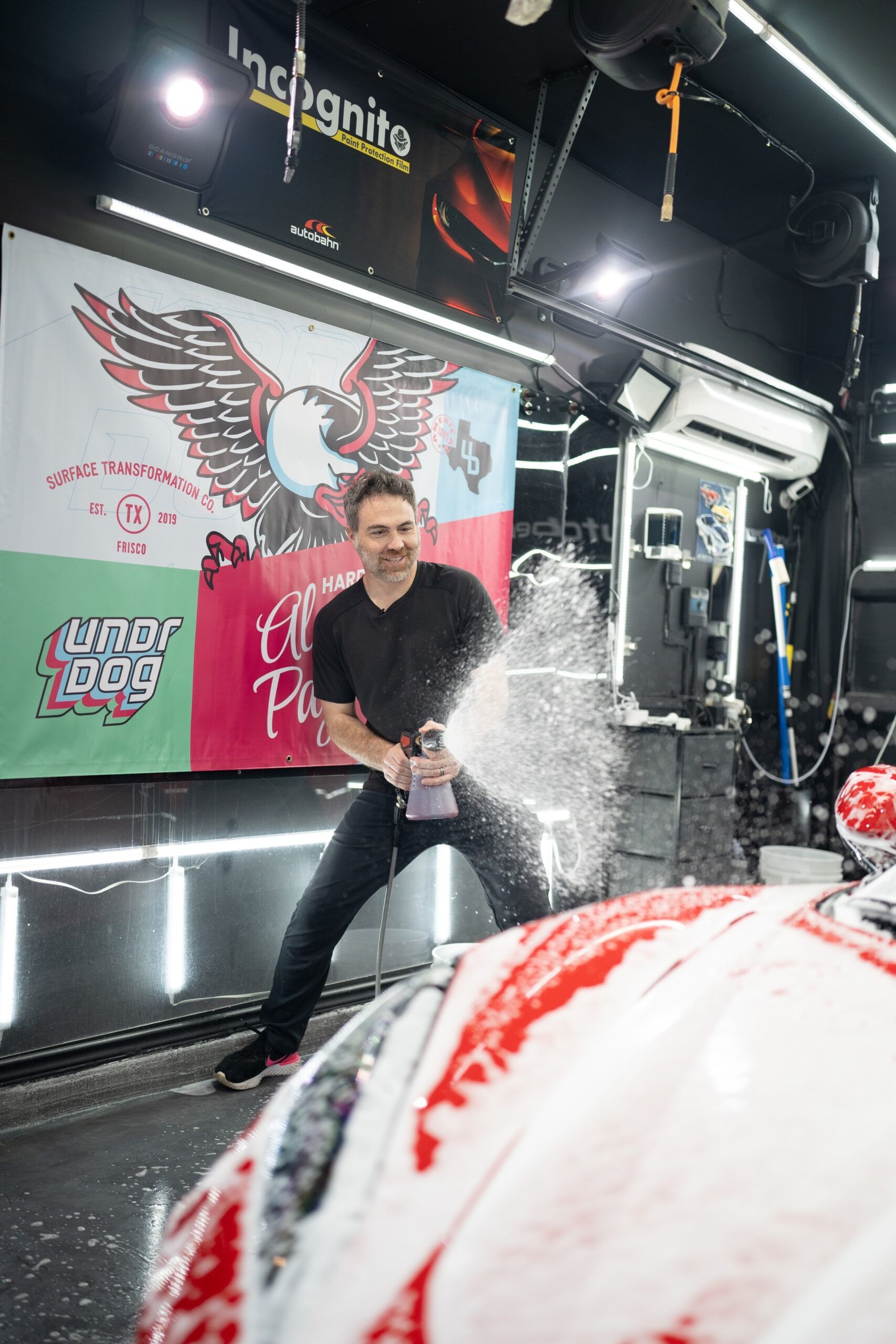A man is spraying foam on a car in a car wash.