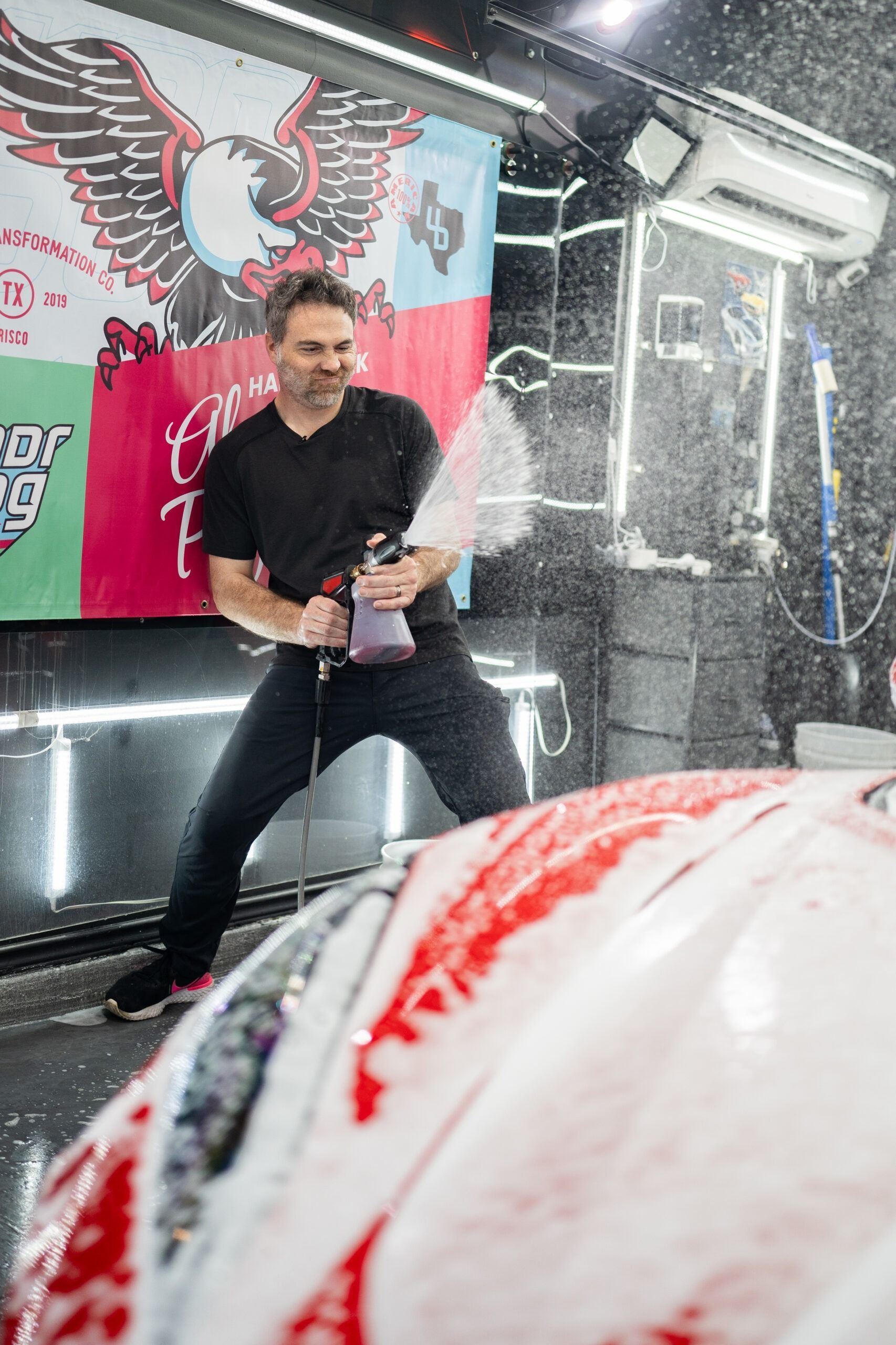 A man is spraying foam on a car in a car wash.