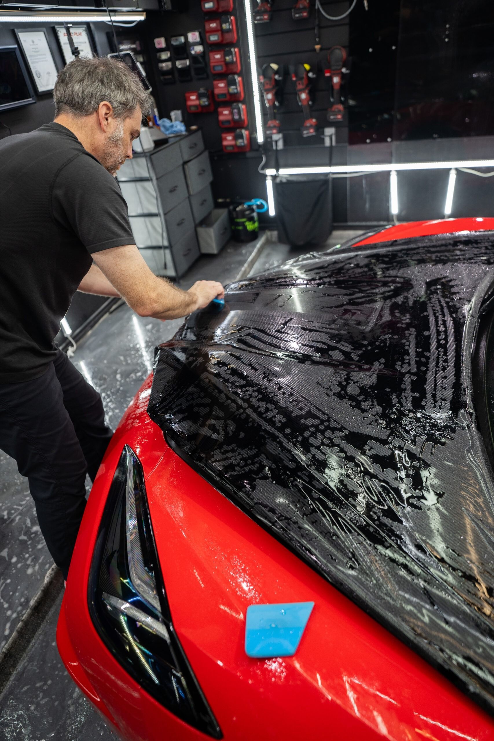 A man is covering the hood of a red car with a black film.