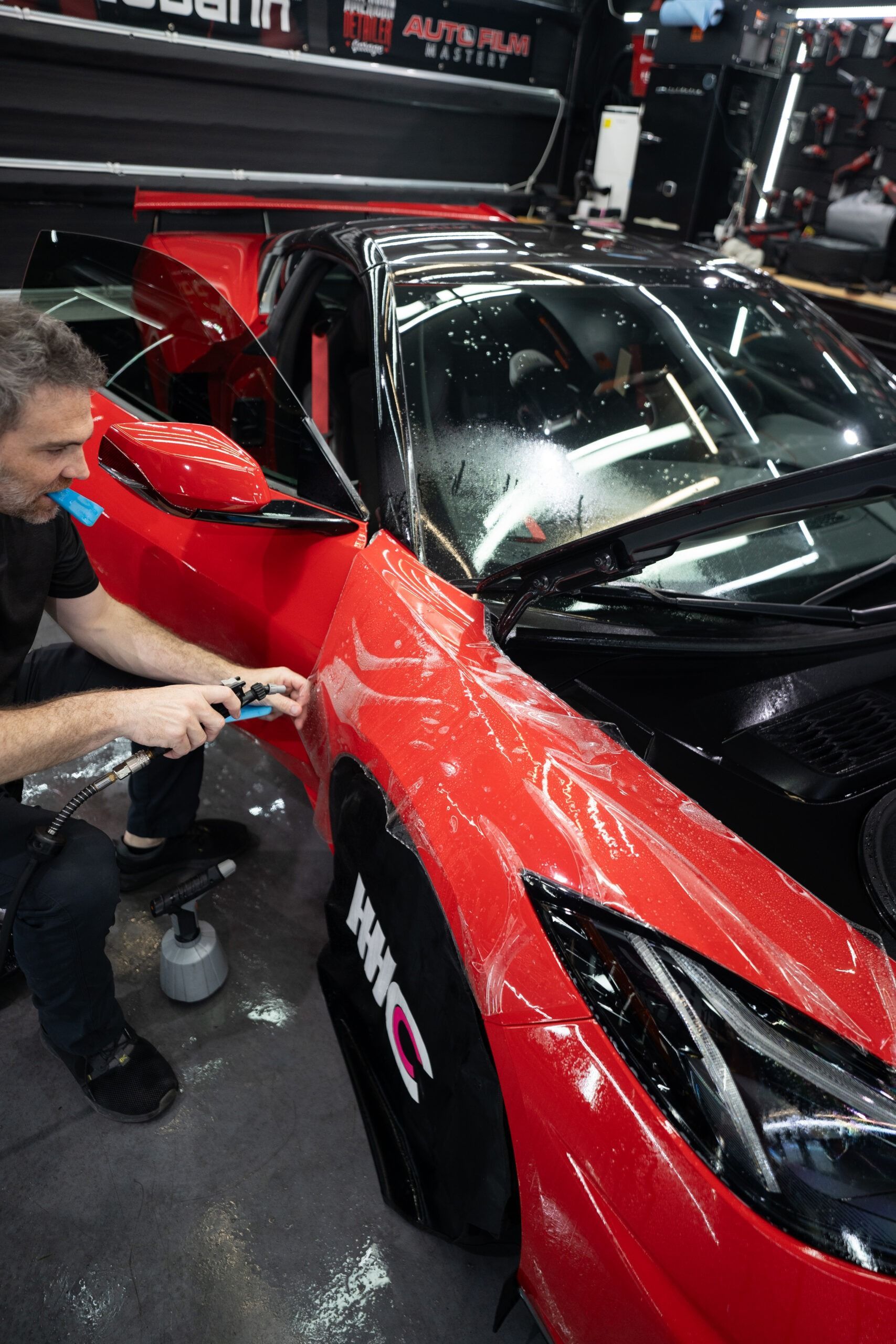 A man is wrapping a red car with plastic wrap.