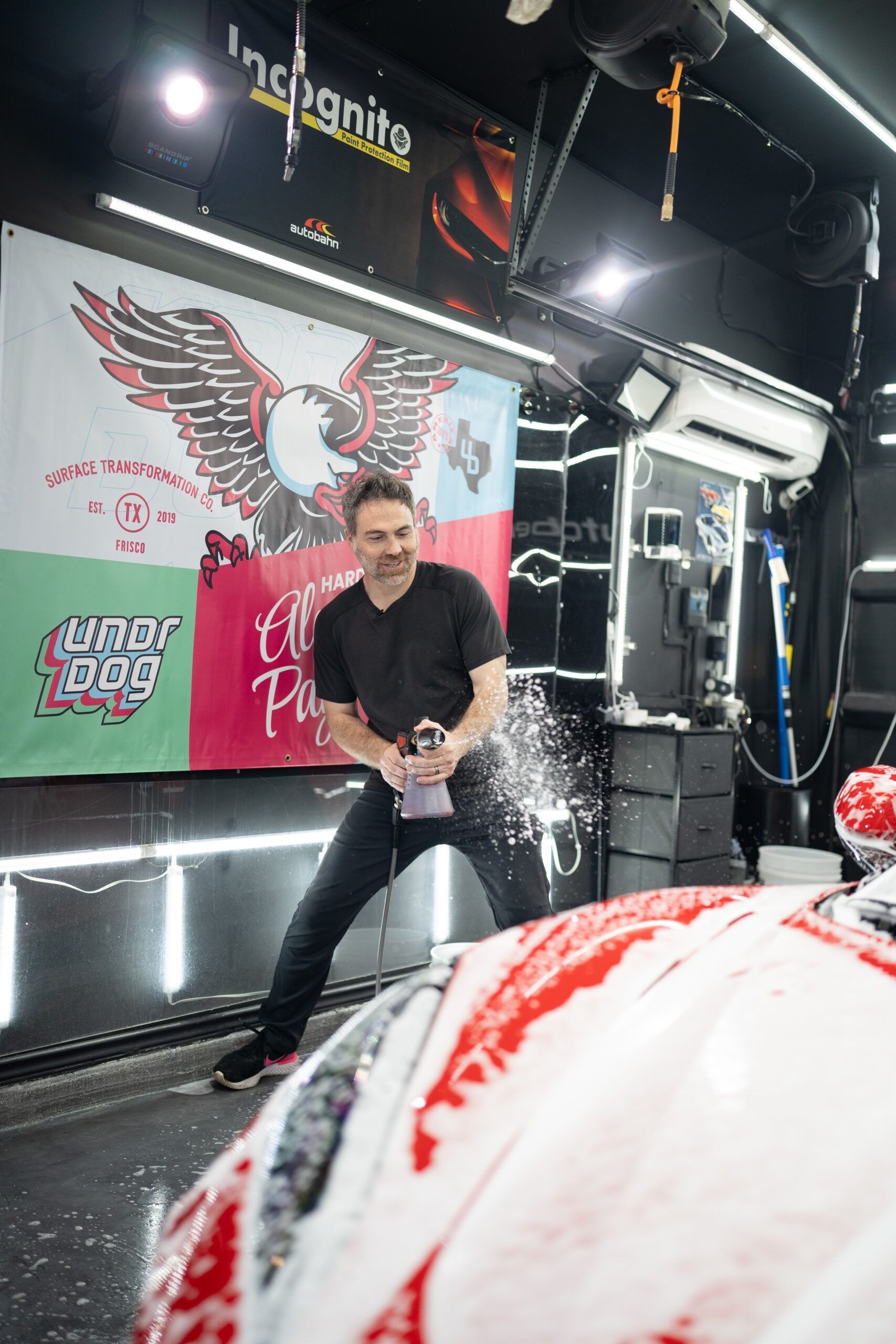 A man is spraying soap on a car in a garage.