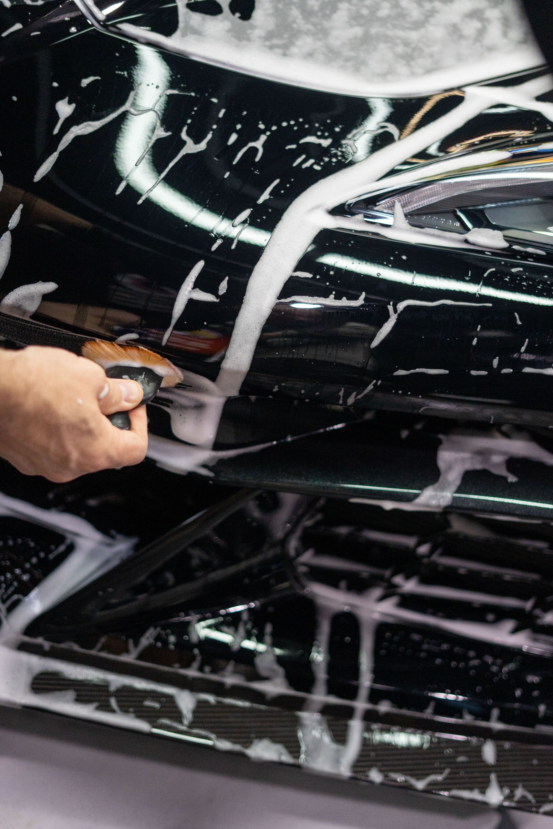 A person is cleaning a black car with a brush.