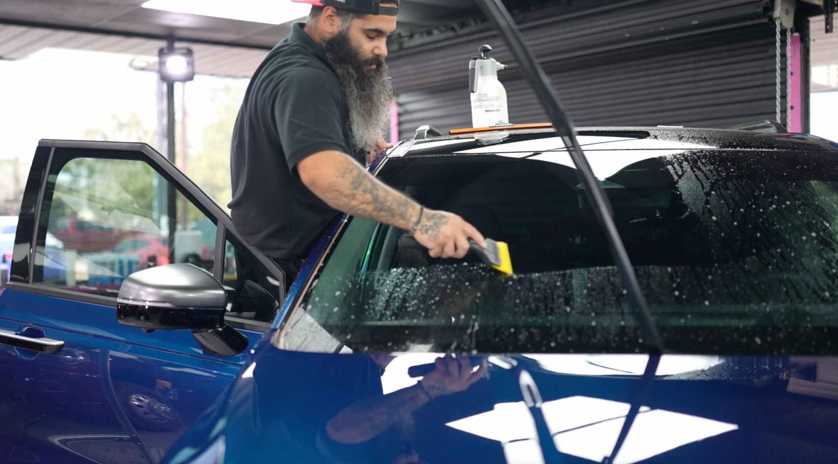 A man with a beard is intalling a window tint of a blue car.