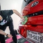A man is cleaning the back of a red car with a sponge.