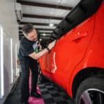 A man is polishing a red car in a garage.