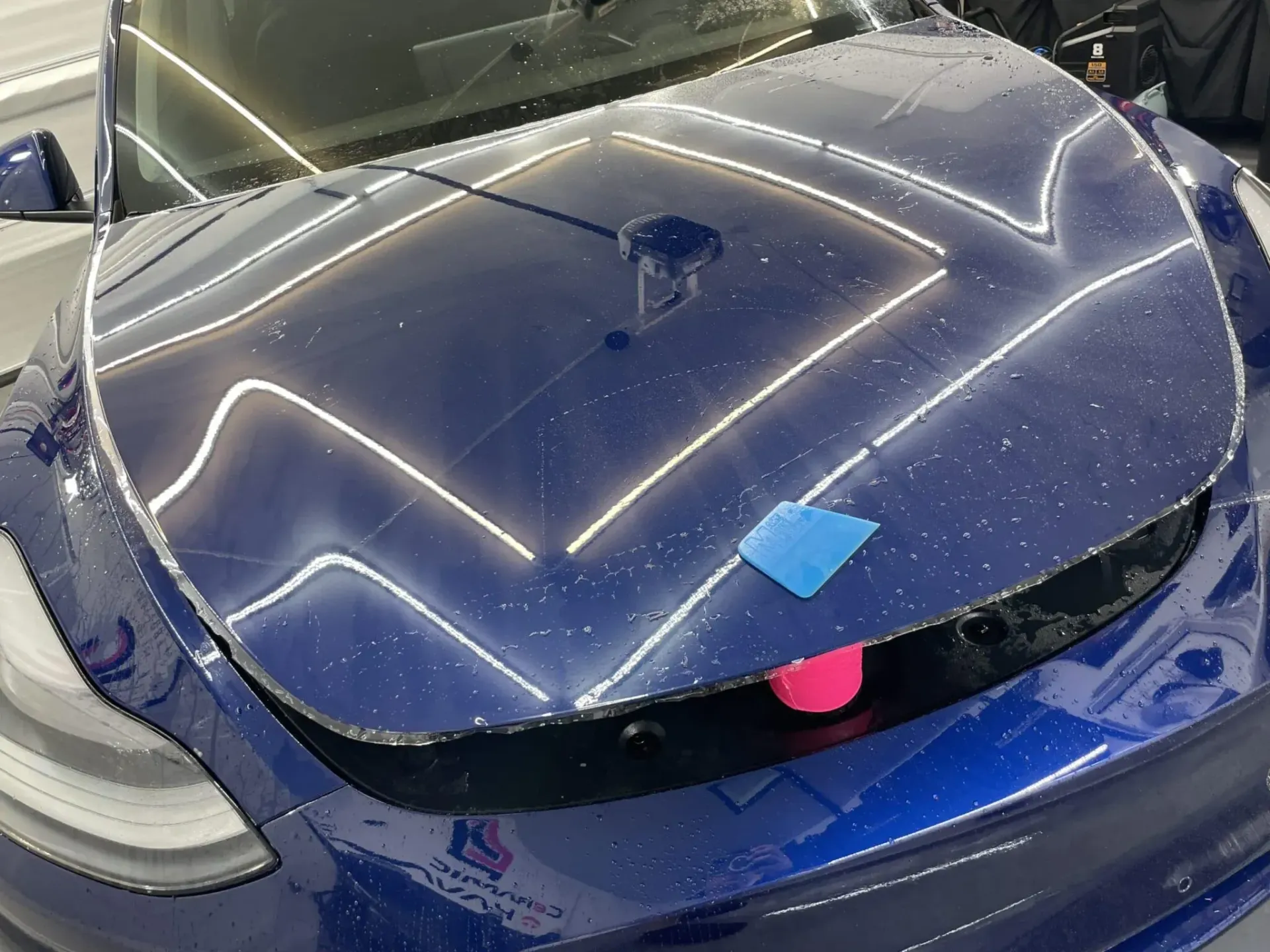A blue tesla model 3 with a blue sticker on the hood