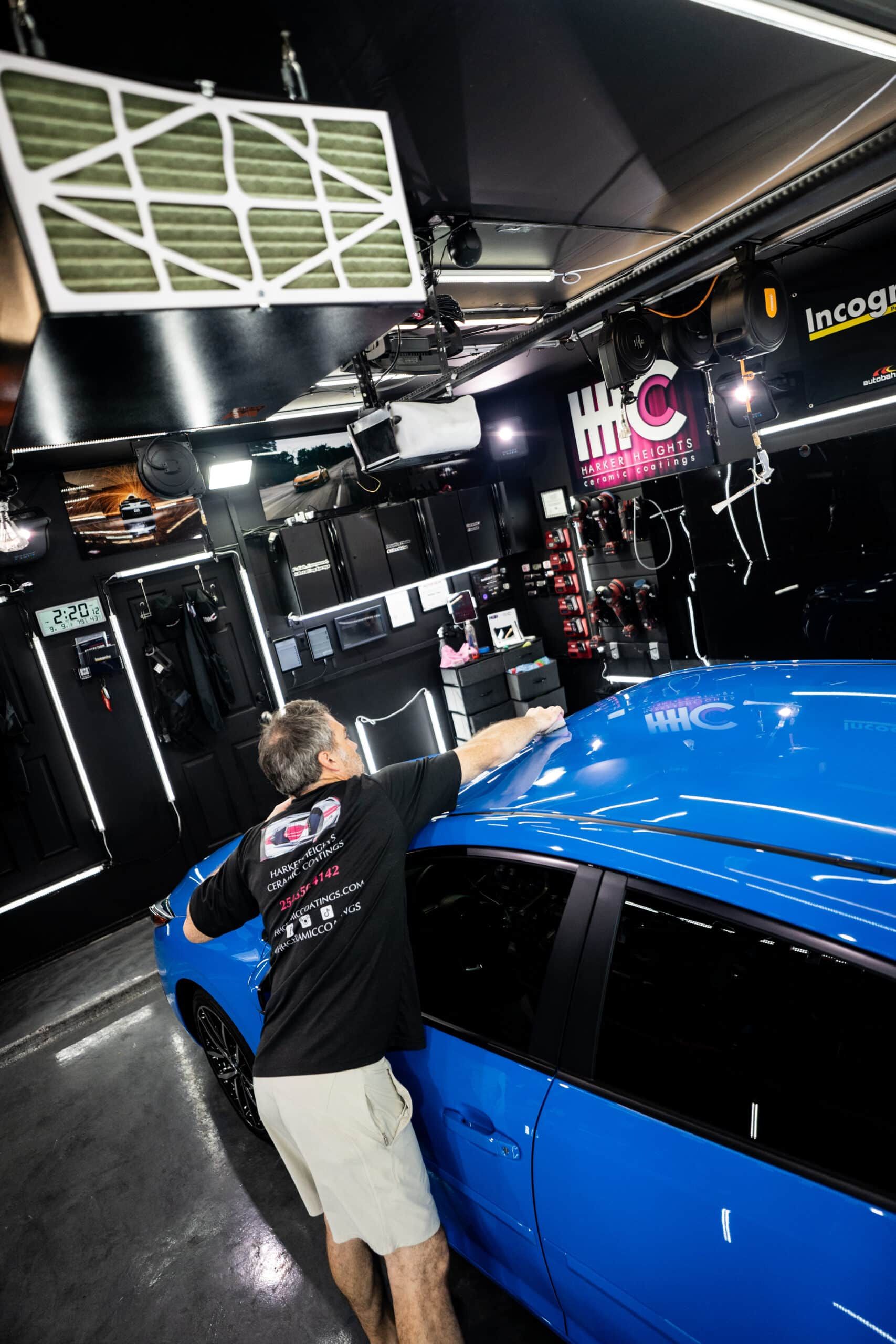 A man is standing next to a blue car in a garage.