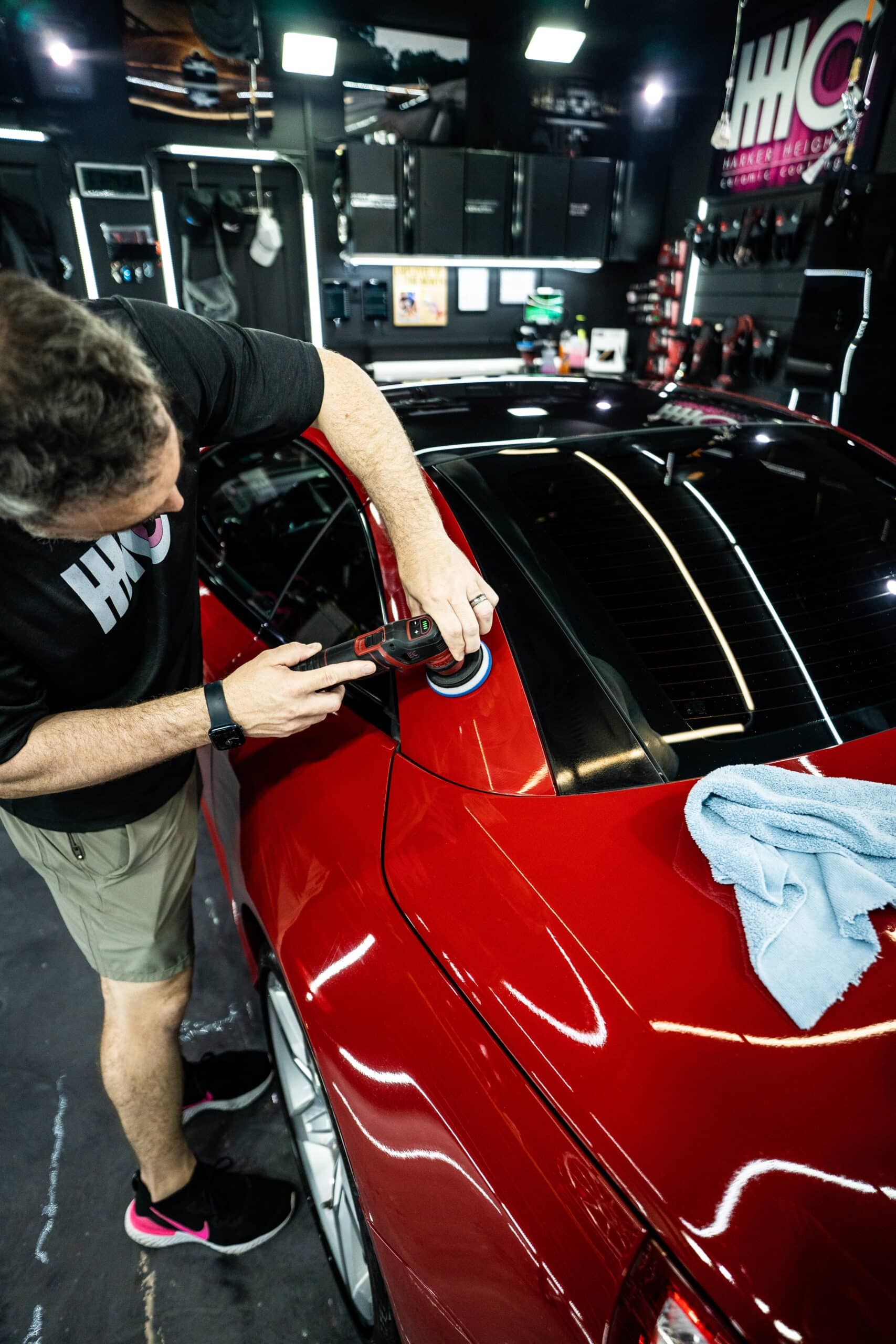A man is polishing a red car in a garage.