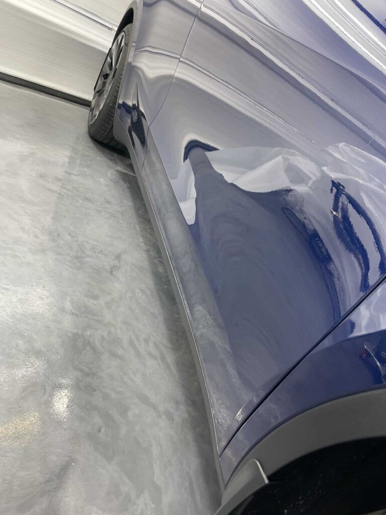 A blue car is parked on a concrete floor in a garage.
