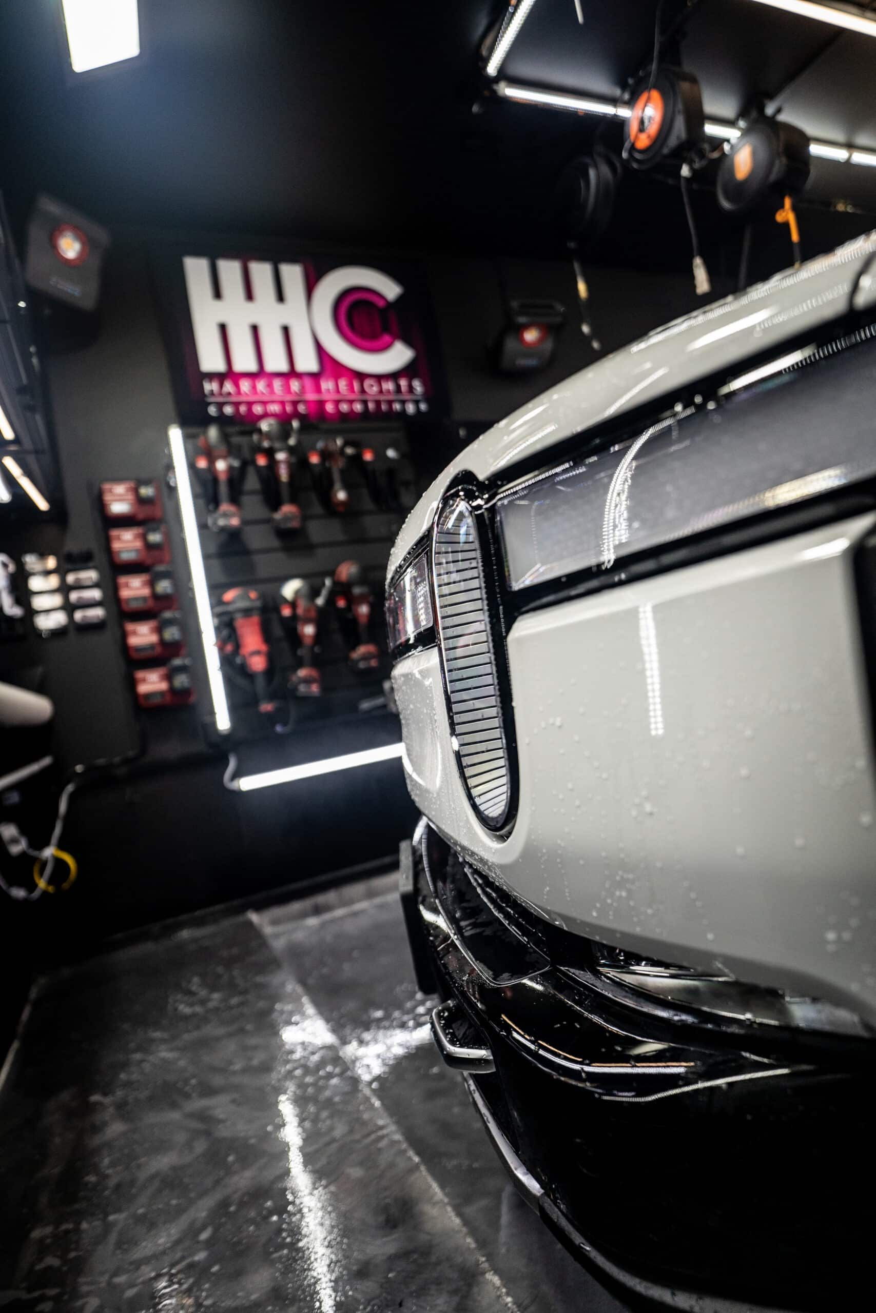 A white car is parked in a garage next to a sign that says hhc.