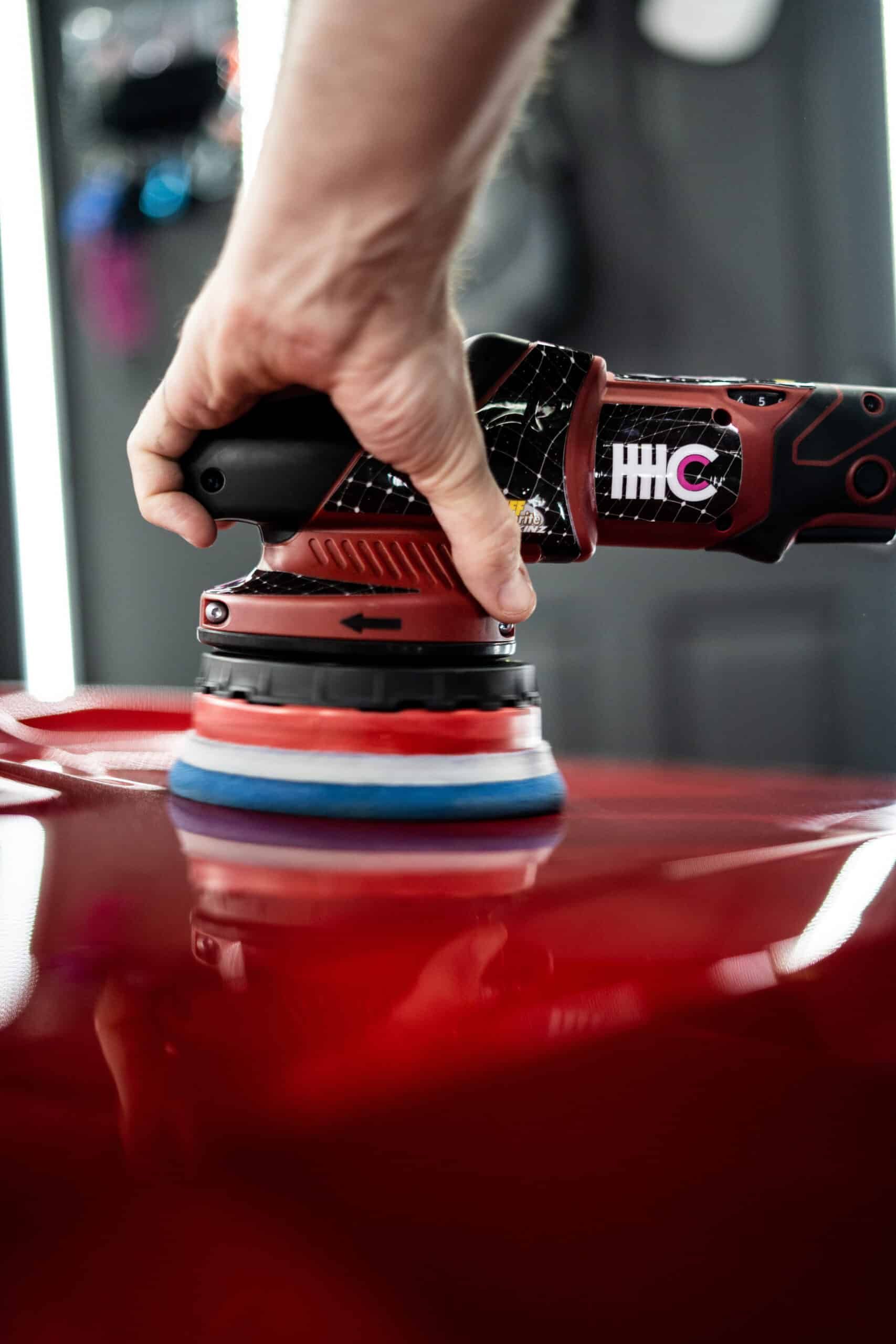 A person is polishing a red car with a machine.