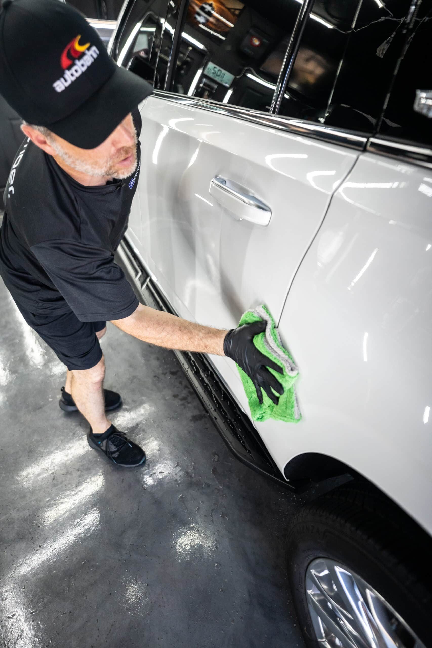 A man is cleaning the side of a white car with a cloth.
