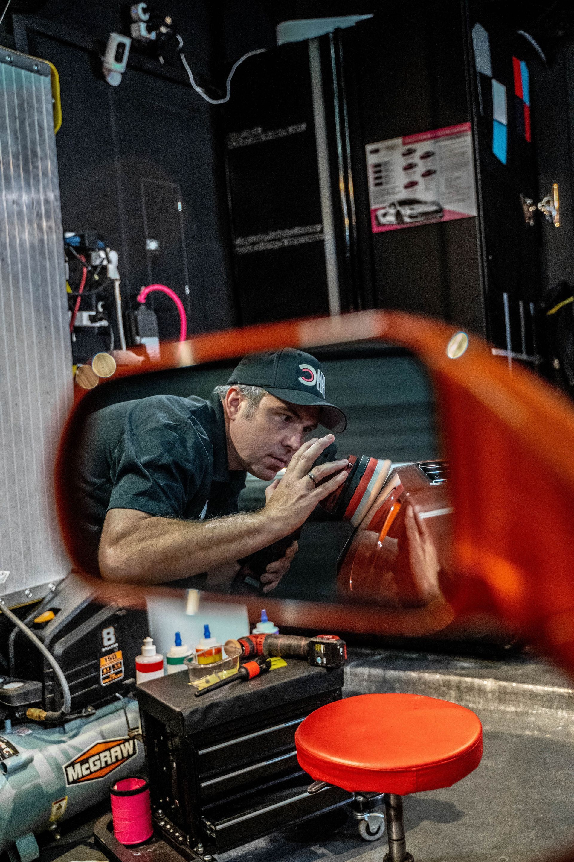 A man is working on a car in a garage in a rear view mirror.