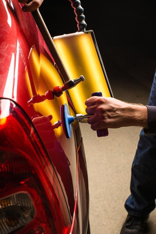 A person using tools to repair a dent on a red car's body.