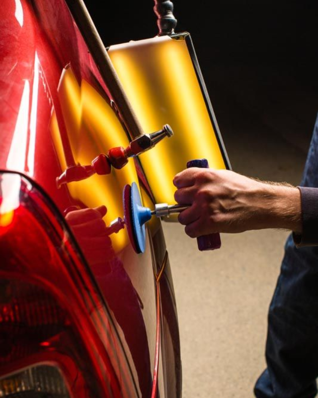 A man is polishing the hood of a red car.