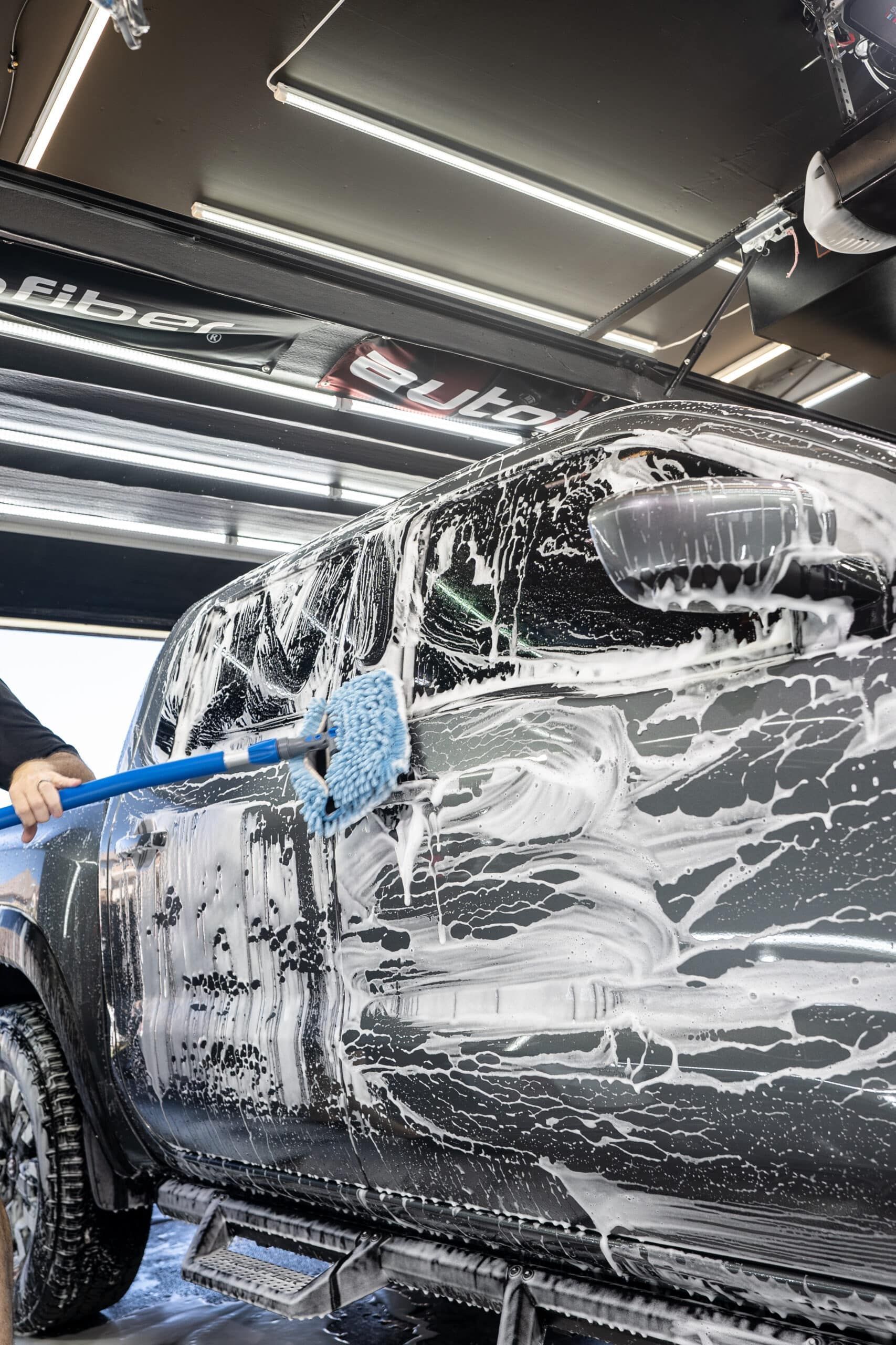 A man is washing a car with foam and a mop.