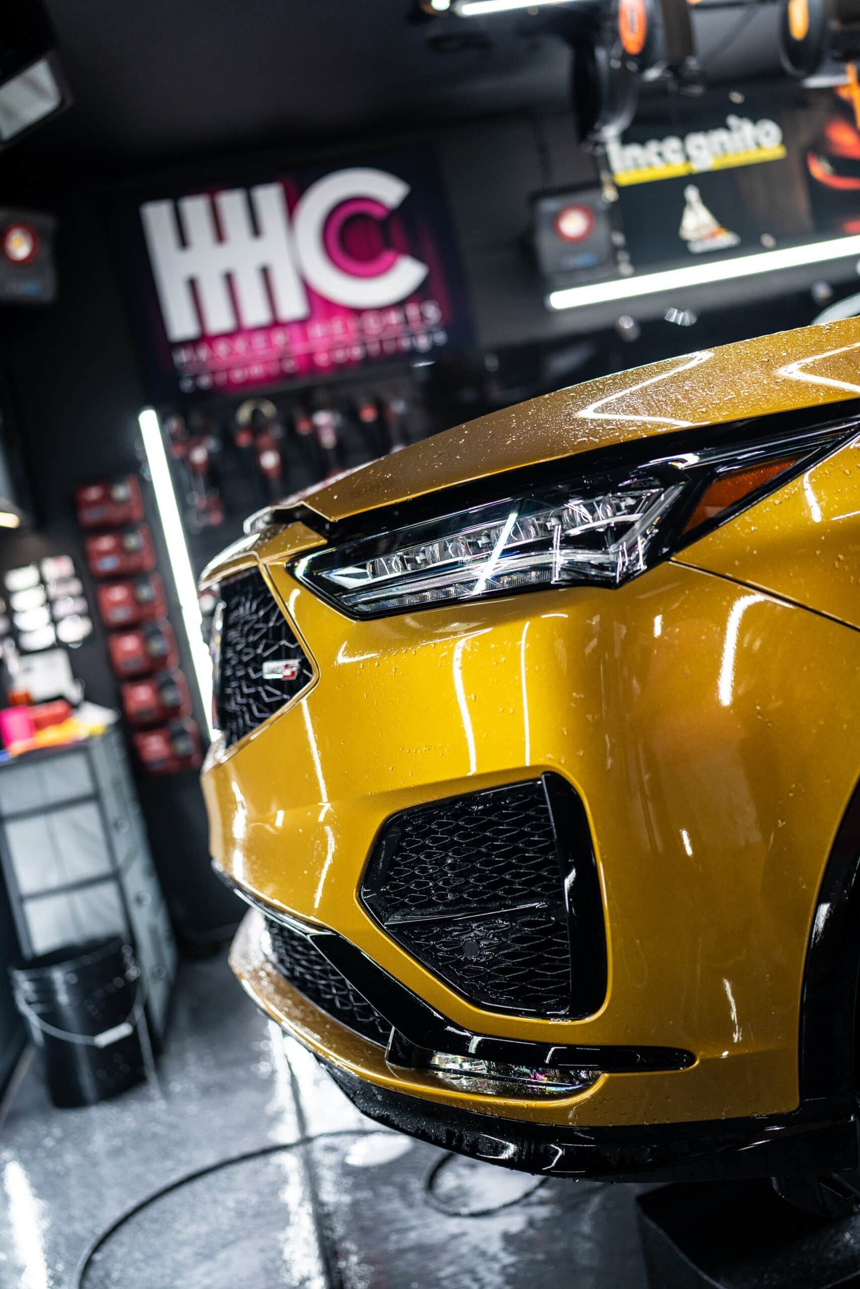 A yellow car is sitting in a garage with a hhc sign in the background.