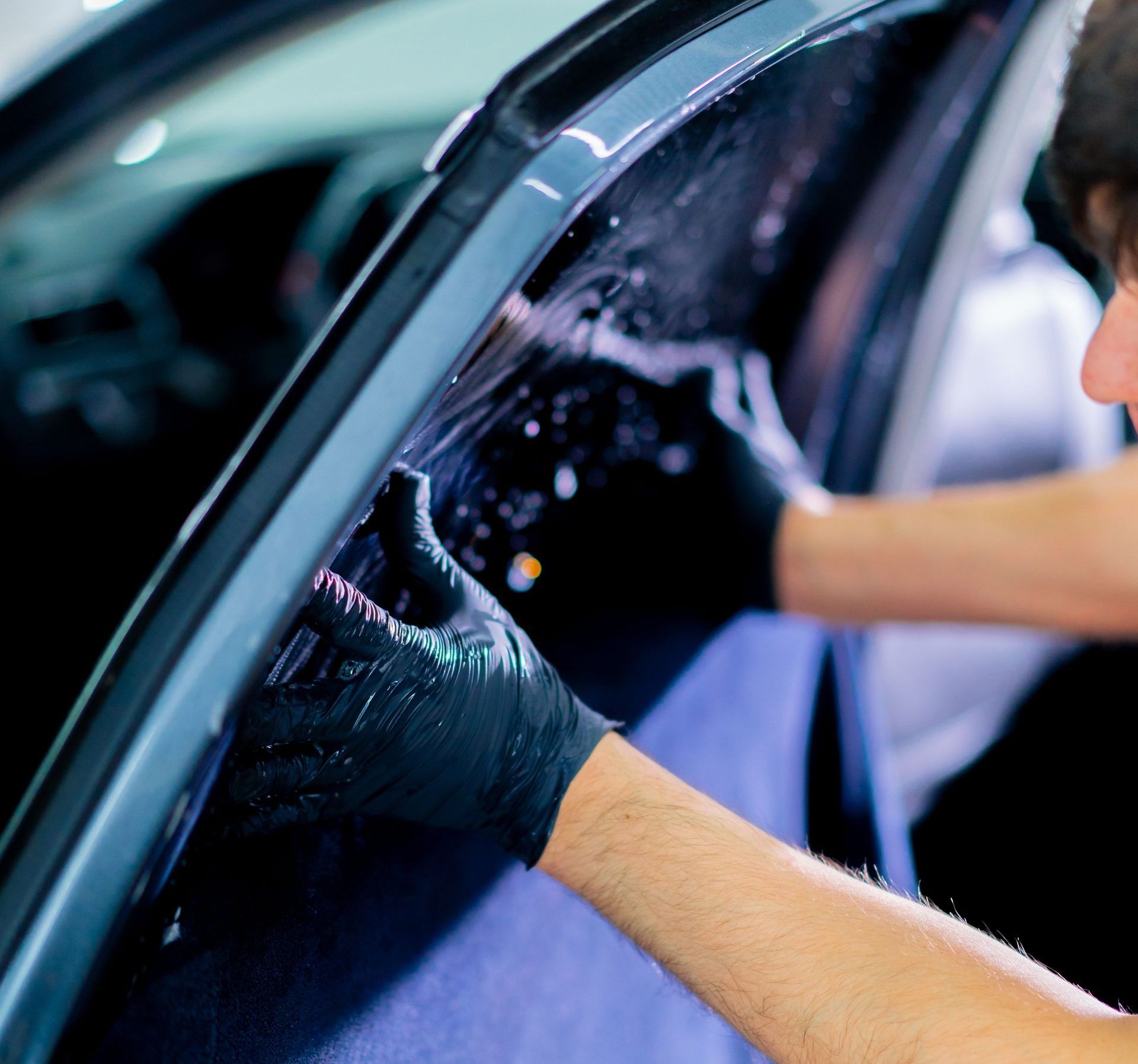 Person wearing black gloves applying window tint to a car window.