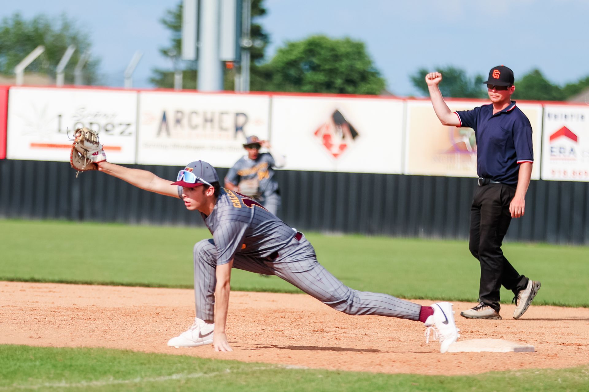 Baseball pitcher in gray uniform delivering a pitch on the mound with umpire signaling behind him.
