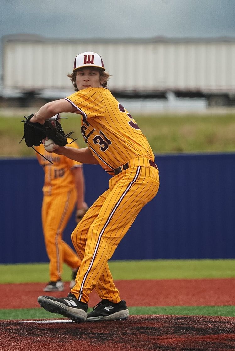 Baseball pitcher in yellow uniform mid-throw on the mound, with an out-of-focus player behind him.