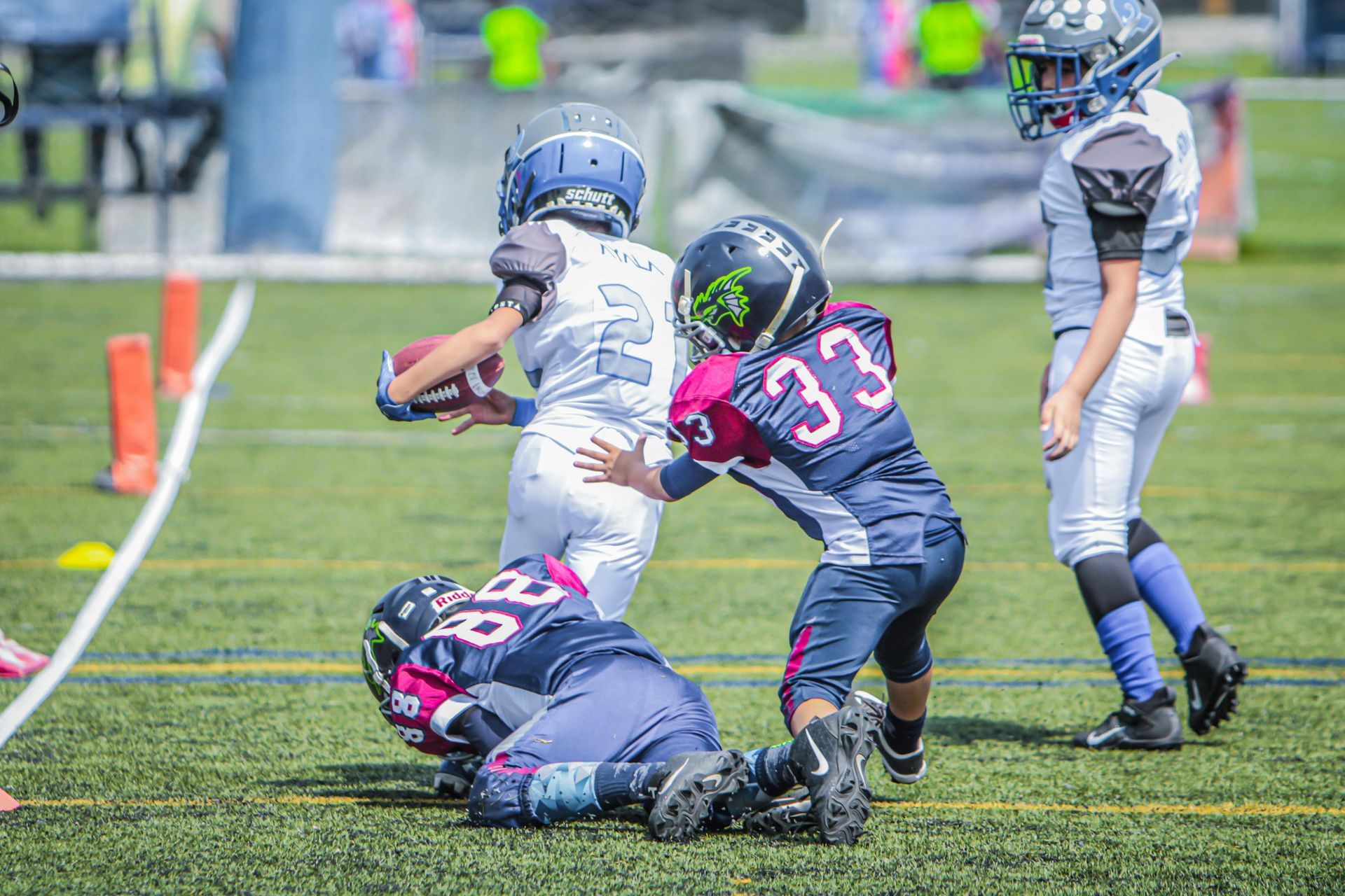 Youth football players tackle on a field, with one player running past defenders.
