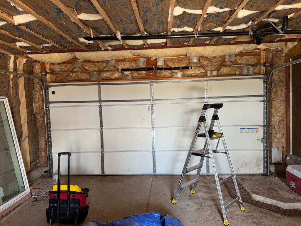 Garage interior with a closed white garage door, open ceiling showing insulation, and a ladder.