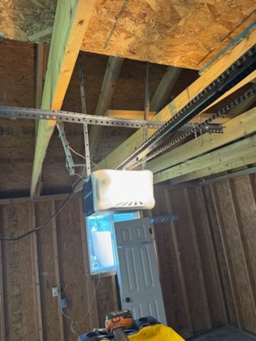 Garage door opener installed on a wood ceiling, with a chain drive and a closed door in the background.