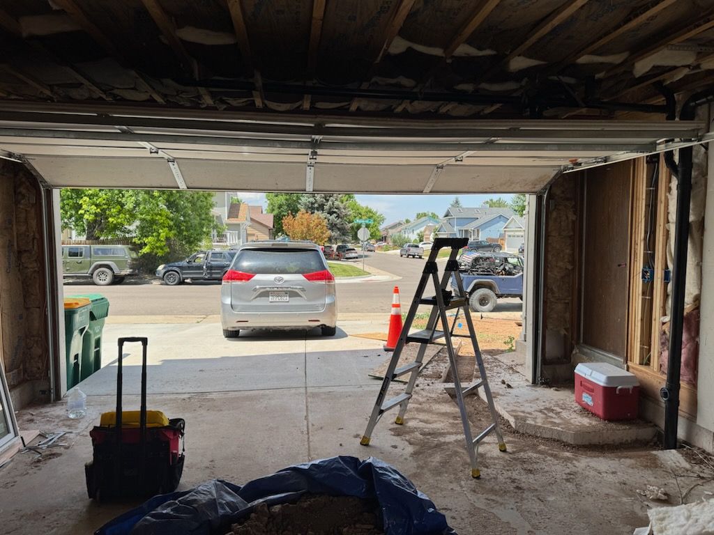 Garage interior with open door, showing vehicles parked on street. A ladder and tools are visible.
