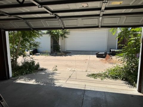 Garage interior looking out at a driveway with a second garage at the end. Trees and brush line the driveway.
