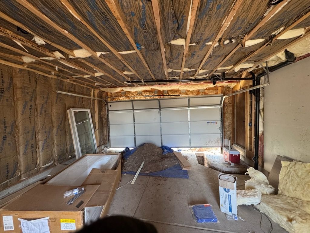 Interior of a garage under construction; insulated walls, garage door at the back, building materials scattered.