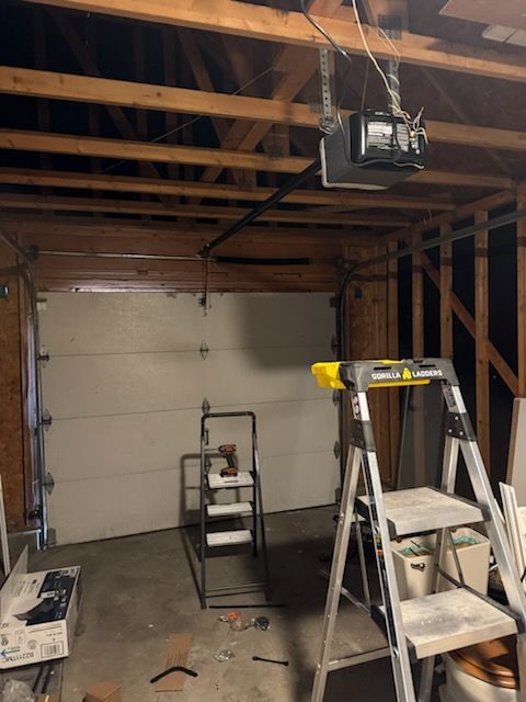 Garage interior with a closed white garage door, ladder, and overhead garage door opener.