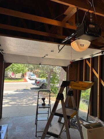 Garage with open door, ladder, and tools; a car and street visible through the opening.