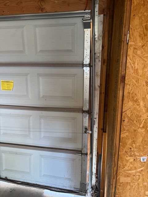 Garage door, white panels, partially open, metal track on right side.