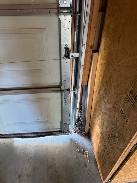 Garage door and track damage at the bottom corner, concrete floor, wooden frame, and a section of paneling.