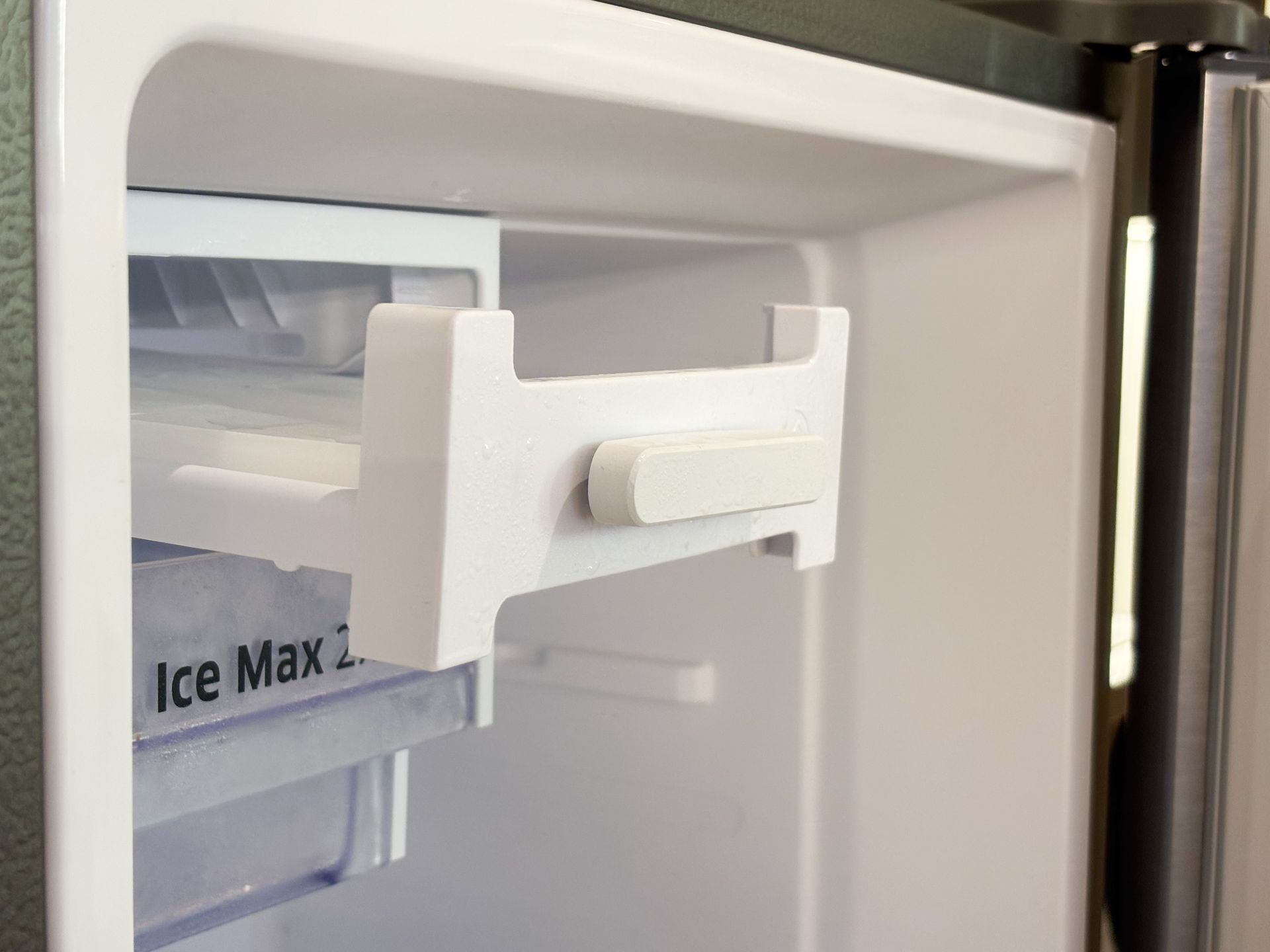 White plastic ice maker mechanism inside a refrigerator, with a bin labeled “Ice Max.”