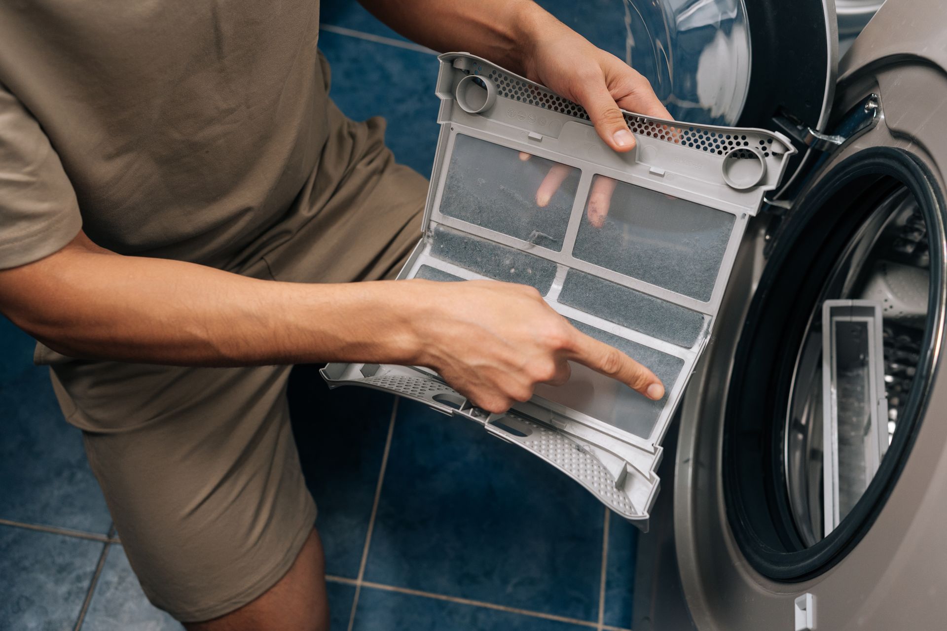 Person cleaning a washing machine filter, pointing to lint buildup inside the appliance