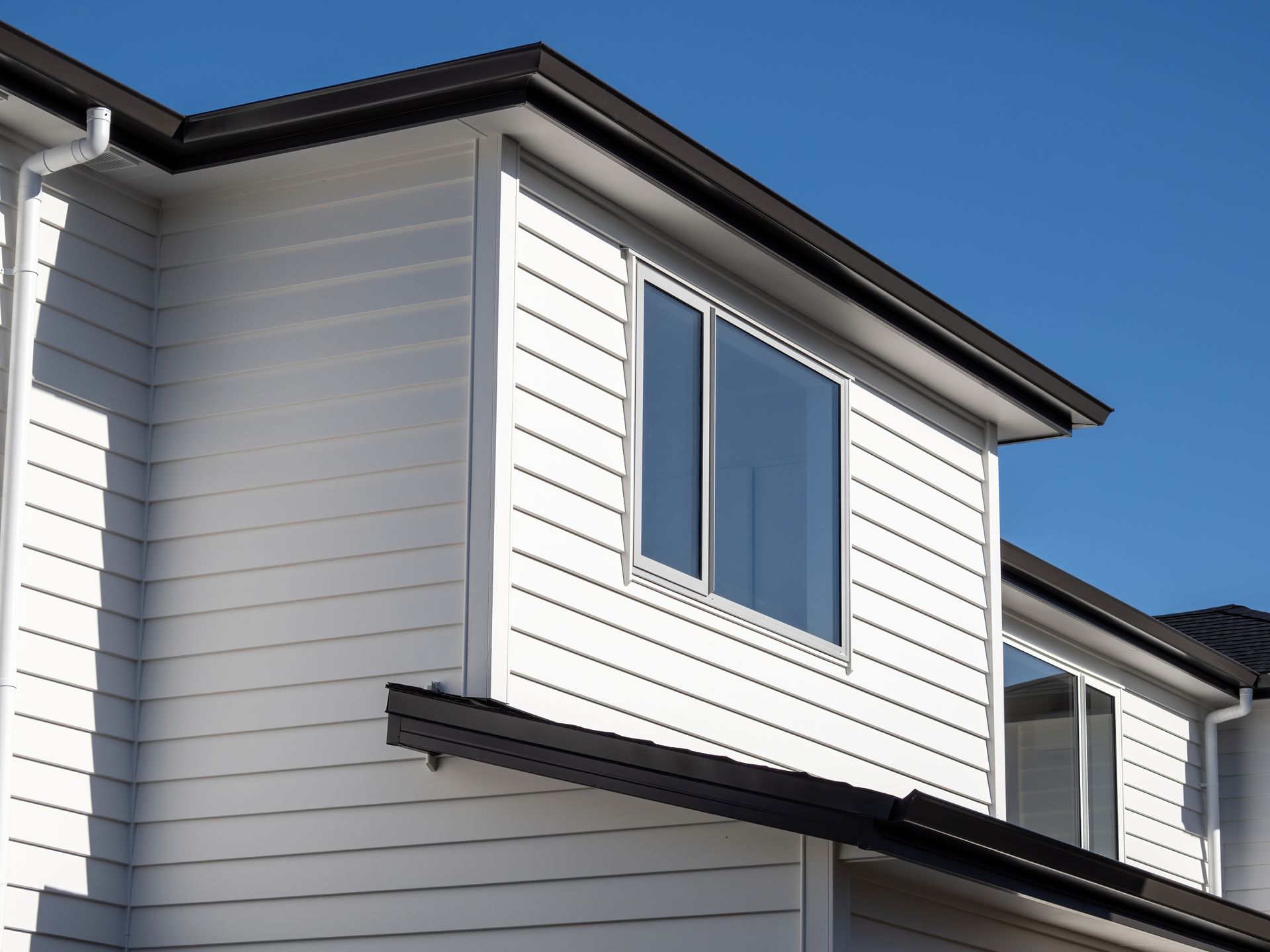 White house exterior with horizontal siding, a dark roof, and a blue-framed window under clear sky