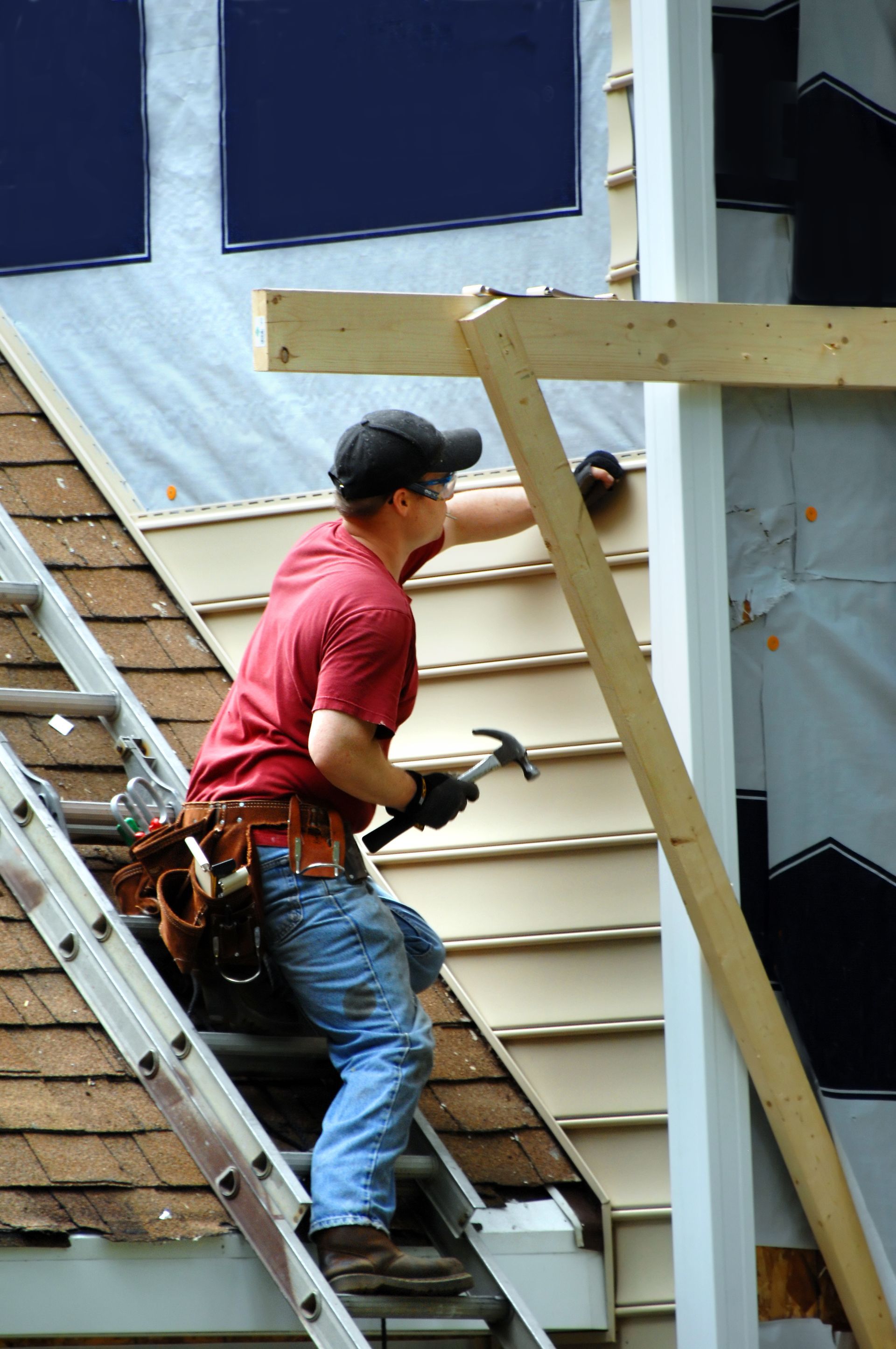 Worker in a red shirt climbing a ladder while installing siding on a house exterior