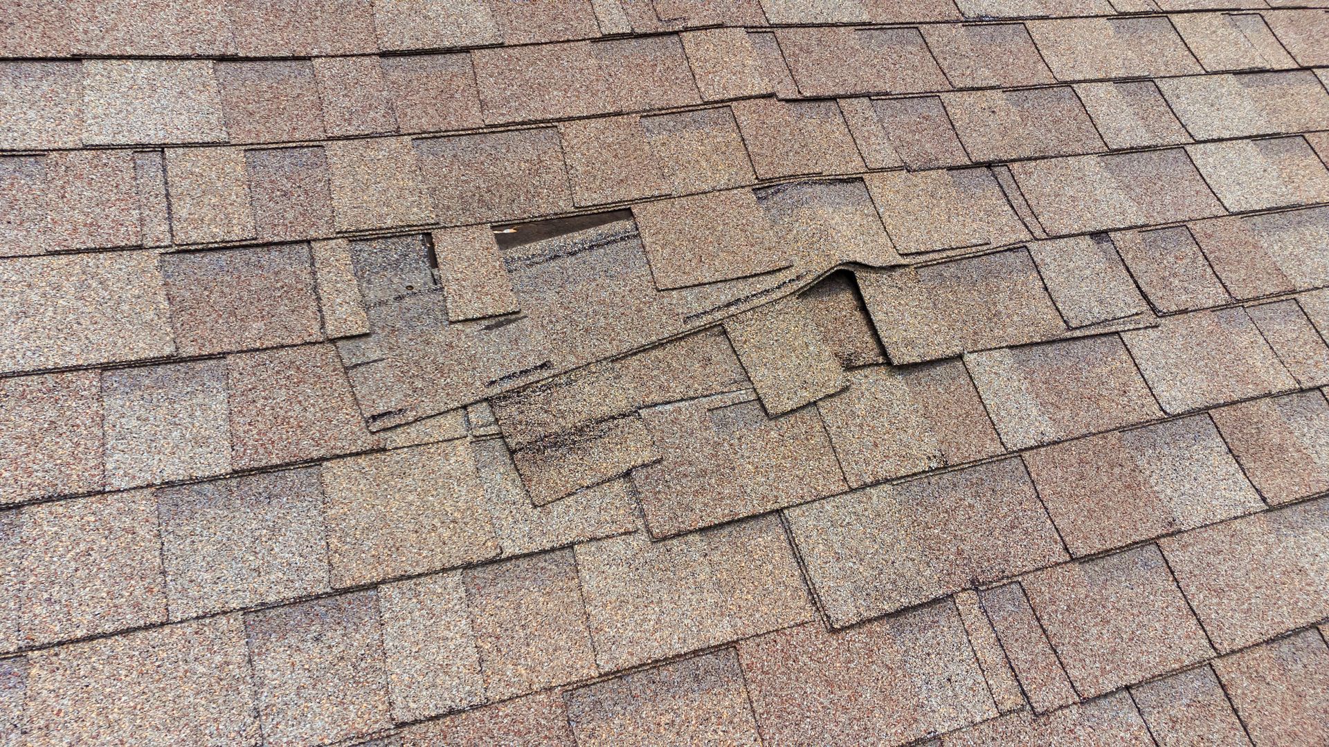 Weathered brown asphalt roof shingles with a few damaged and missing pieces