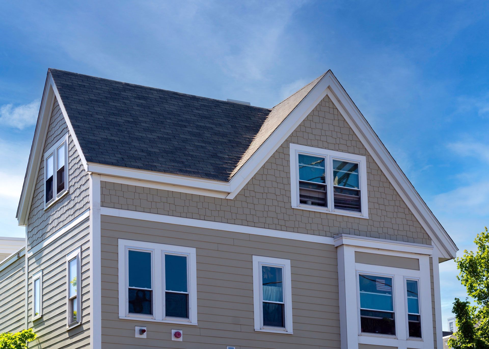 Tan two-story house with gray roof and blue sky background.