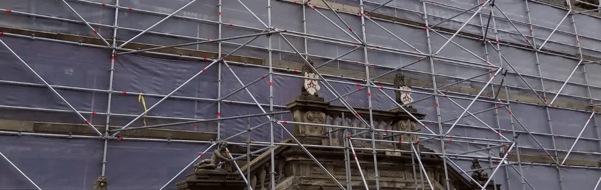 Een groot gebouw is bedekt met steigers en zeilen.